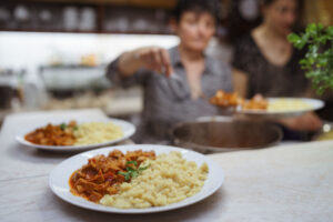 rissen tálalt meleg étel egy rendezvényen, háttérben a felszolgálás folyamatával – professzionális esemény- és gasztrofotózás a FotoFilo-tól.