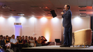 Motivációs előadás a Generációk Bölcsessége rendezvényen, háttérben a figyelő közönséggel – professzionális eseményfotózás a FotoFilo-tól.